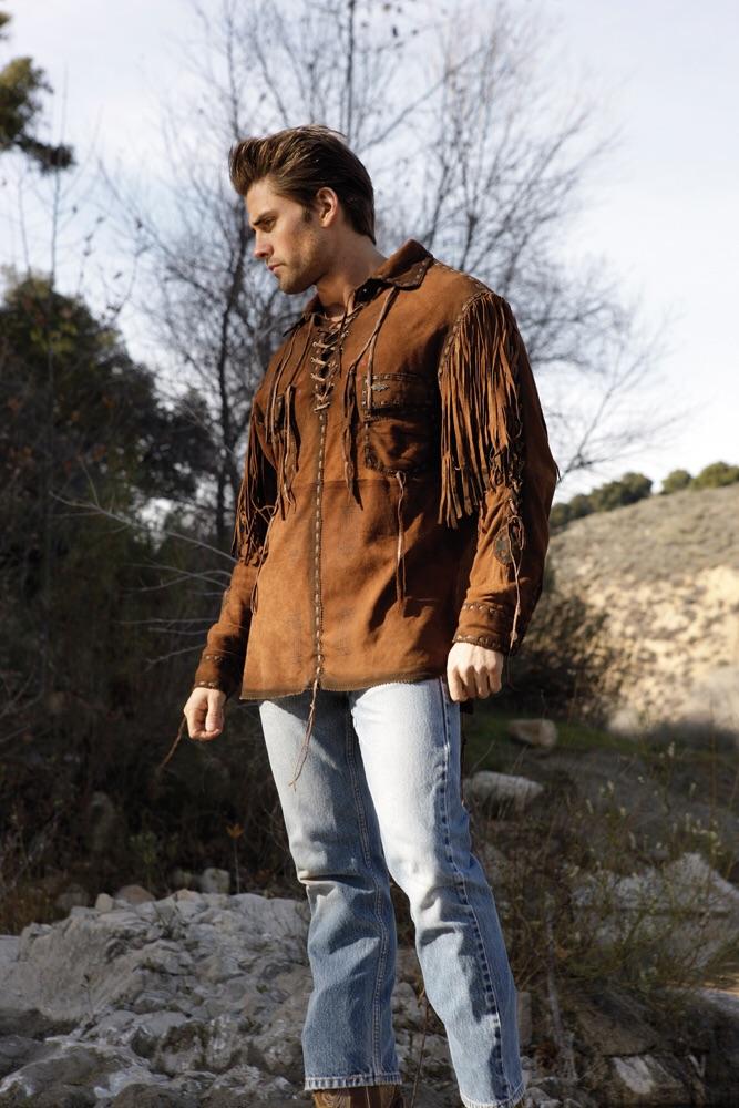 Man wearing a brown suede fringe jacket and light blue jeans standing outdoors.