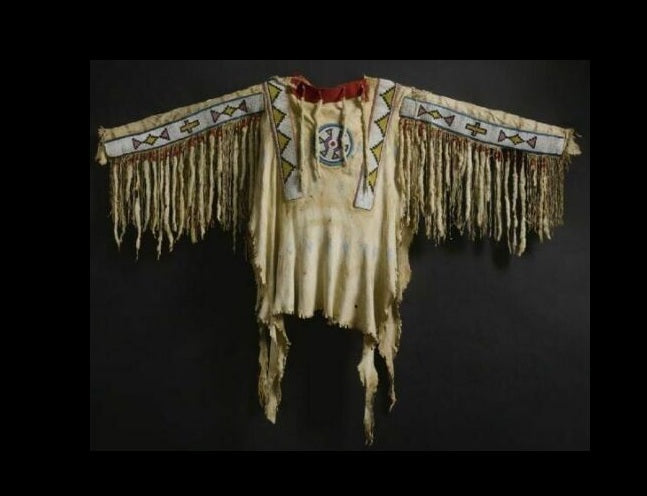 Traditional Native American garment with intricate patterns and fringes on a dark background