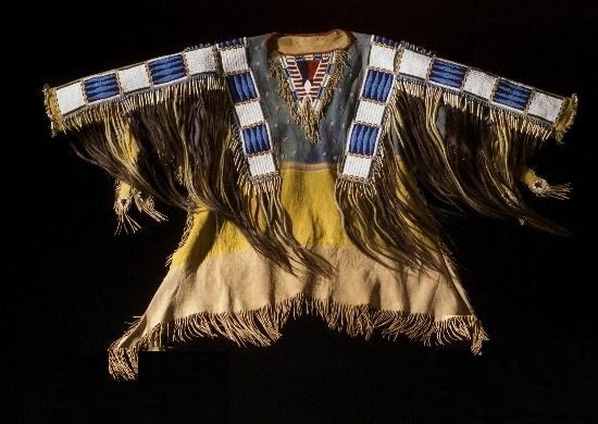 Traditional Native American garment with fringes and patterns on a black background