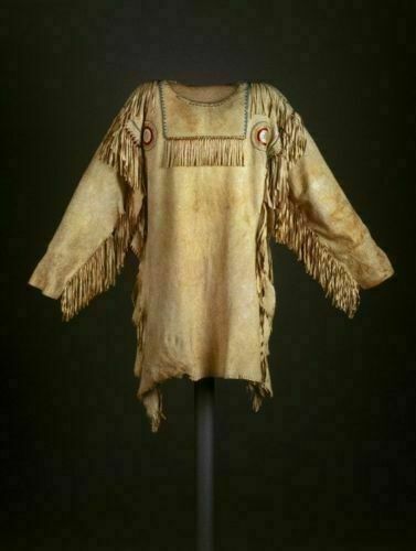 Traditional Native American garment with fringes and beadwork on a dark background
