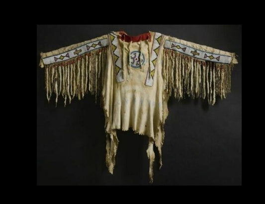 Traditional Native American garment with intricate patterns and fringes on a dark background