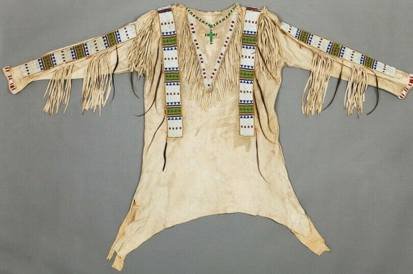 Traditional Native American garment with fringes and beadwork on a gray background