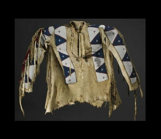 Traditional Native American garment with intricate patterns and fringes on a dark background